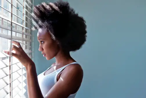 Young woman looking out of blinds (horizontal)